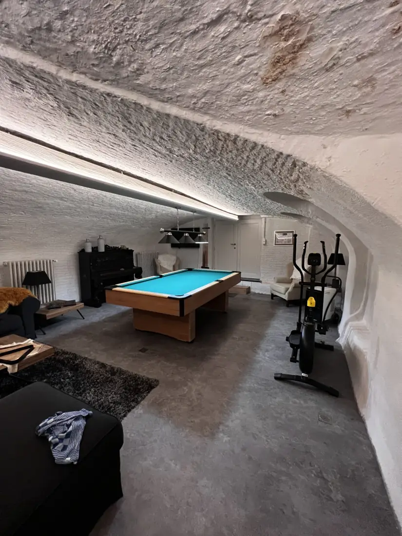 De afgewerkte mancave in Brugge met biljart, piano en fitnesstoestel onder een wit tongewelf